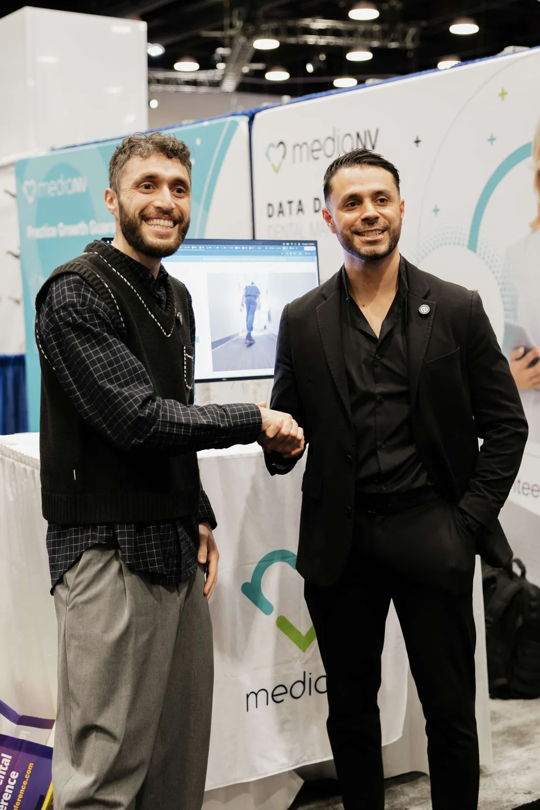 Two MediaNV team members shaking hands at the company's conference booth