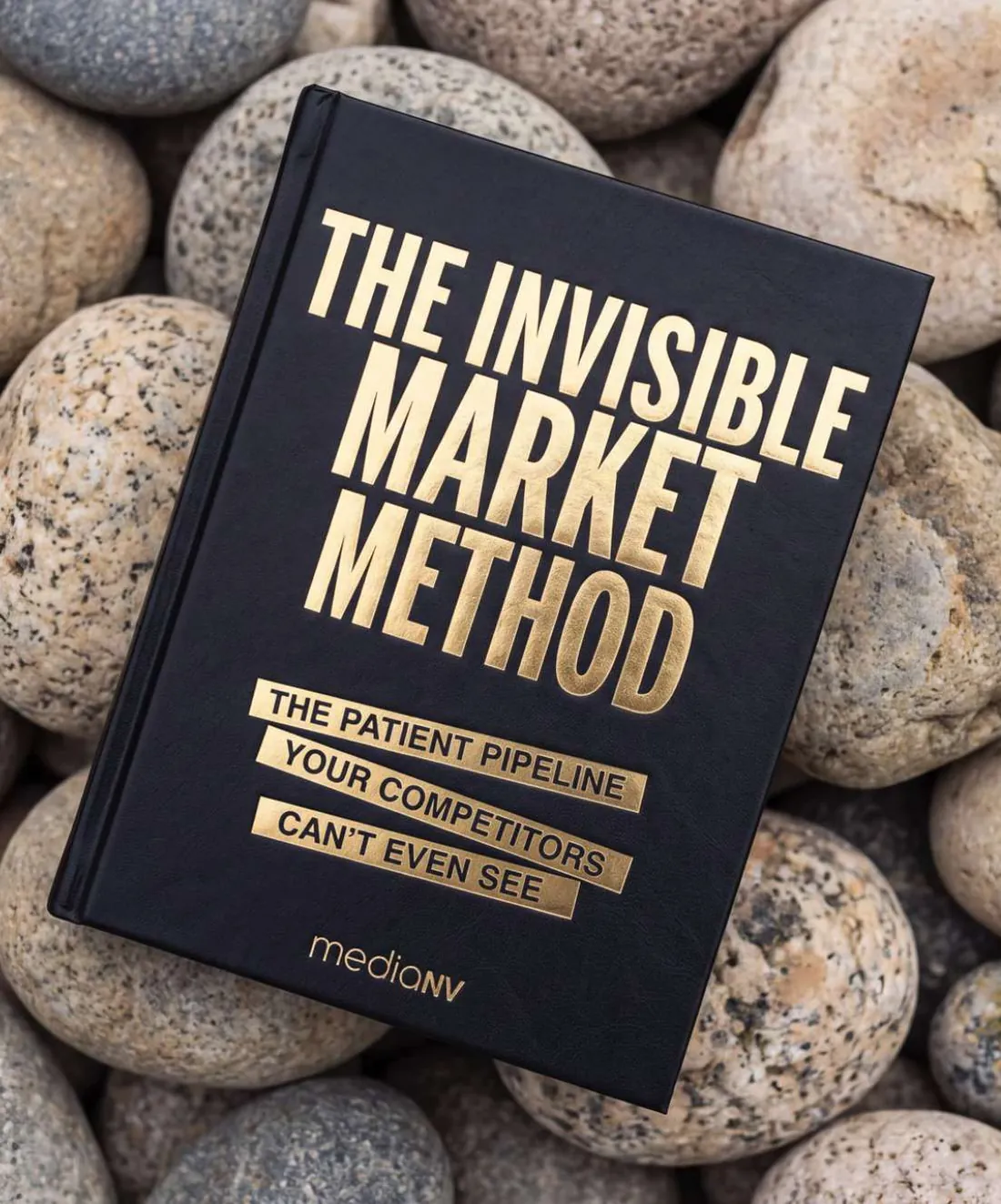 The Invisible Market Method book resting on smooth grey stones
